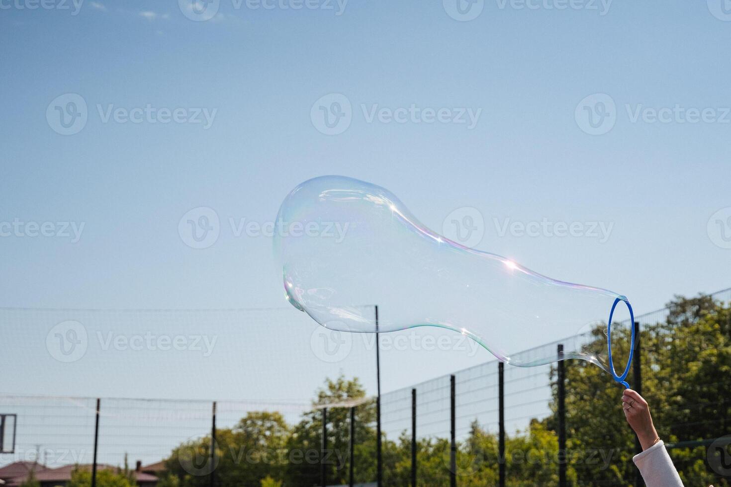 A colorful soap bubble floats against a clear blue sky at a sunny playground, evoking joy and nostalgia for carefree childhood moments filled with playful activities with friends and family photo