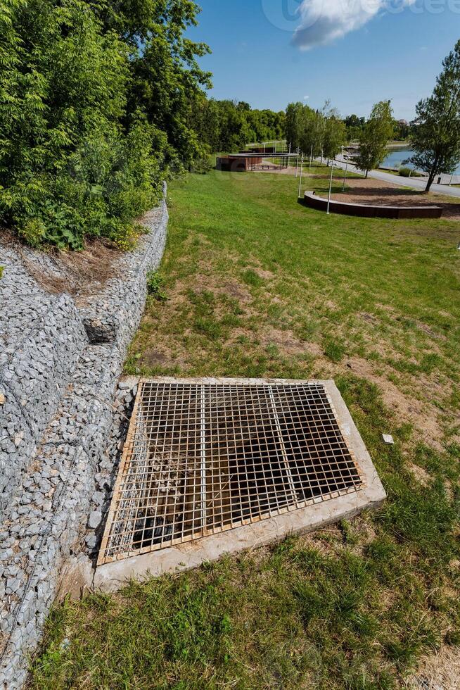 A manhole cover can be seen currently resting in the grass right next to a sturdy rock wall, creating a unique and interesting contrast between natures beauty and urban infrastructure photo