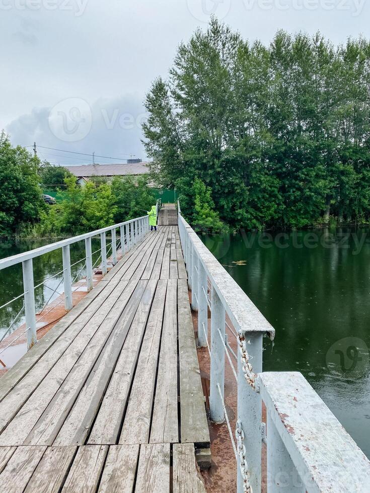 A charming wooden bridge gracefully spans over a tranquil body of water, surrounded by lush trees that provide shade and beauty to the scene, creating a picturesque landscape photo