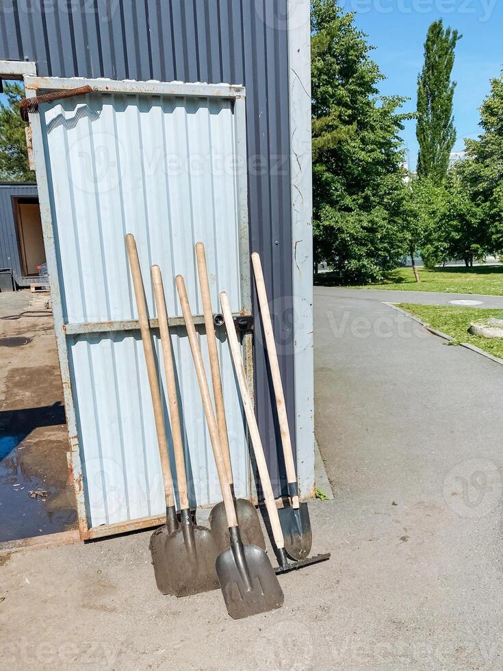 A collection of various shovels is resting on the ground just in front of a building, perhaps patiently awaiting to be used for an upcoming gardening project or other landscaping activities photo