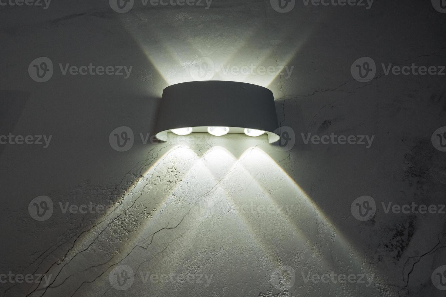 A bright and stylish white wall light is beautifully shining on a contrasting dark wall, creating an interesting play of shadows and illumination that enhances the ambiance of the room photo