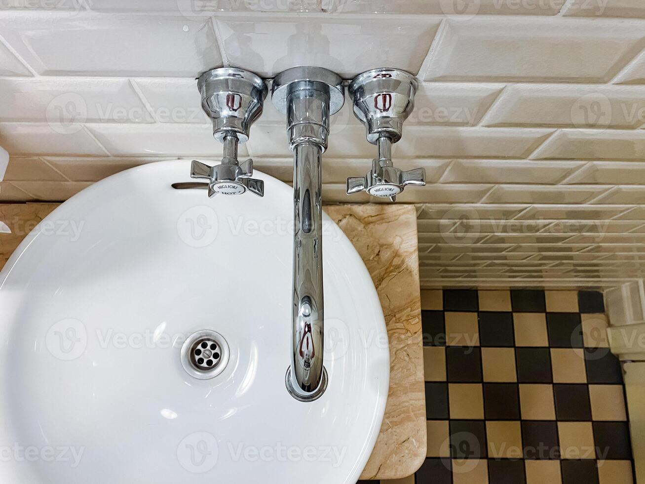 In this bathroom, there is a unique sink featuring three distinct faucets, complemented by an eyecatching checkered floor design that enhances the overall aesthetic appeal of the space photo
