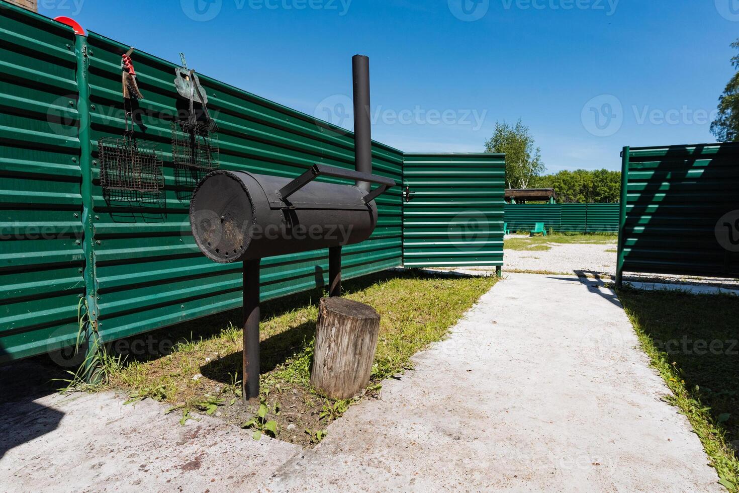 In a serene backyard, a sleek black grill stands out among lush green fencing, inviting summer cooking and relaxation under a clear blue sky, perfect for gatherings with friends and family photo