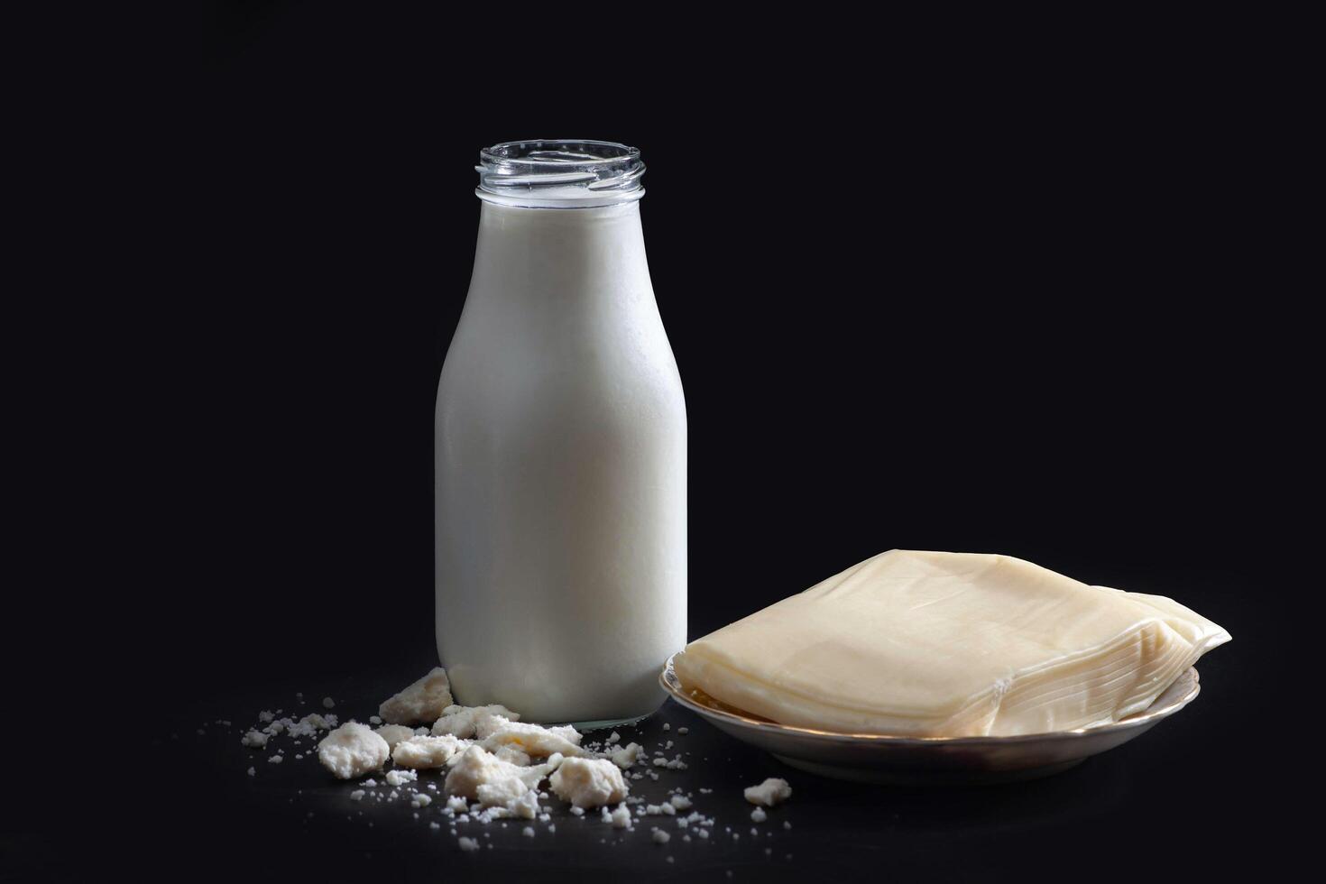 A bottle of milk and a piece of cheese on a black background photo