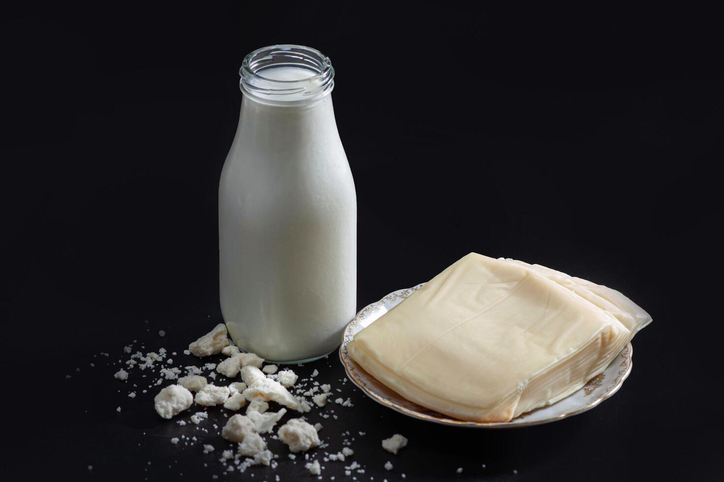 A glass bottle of milk and a piece of cheese photo