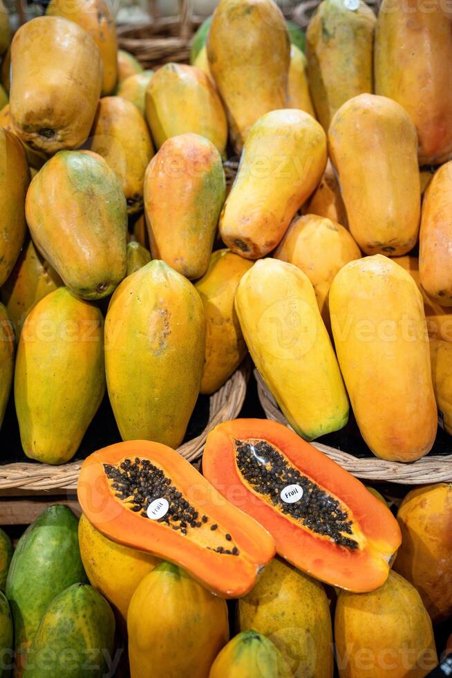 Halved fresh papaya with black seeds and price tag fills foreground at market stall. Full frame photo
