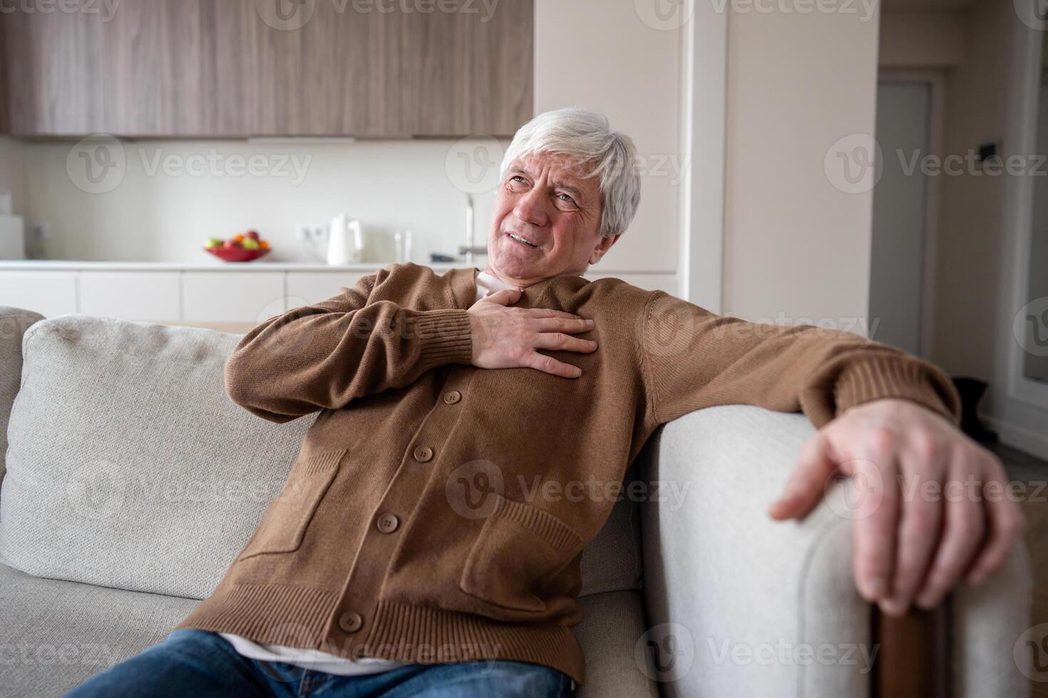 Distressed old man in pain suffers on sofa clutching chest, myocardial infarction heart attack photo