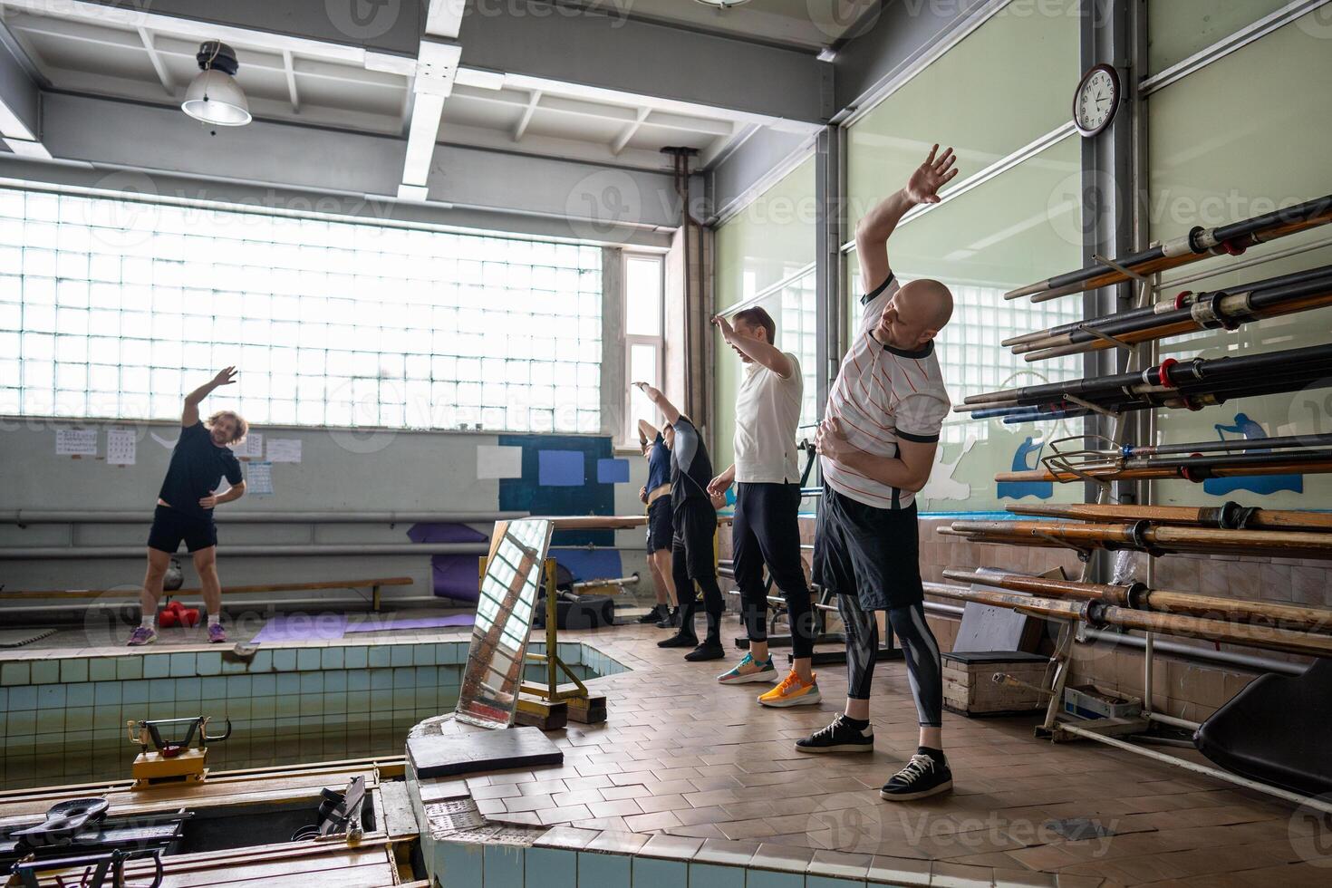 Determined concentrated athlets execute side bend under coach guidance, preparing for rowing workout photo