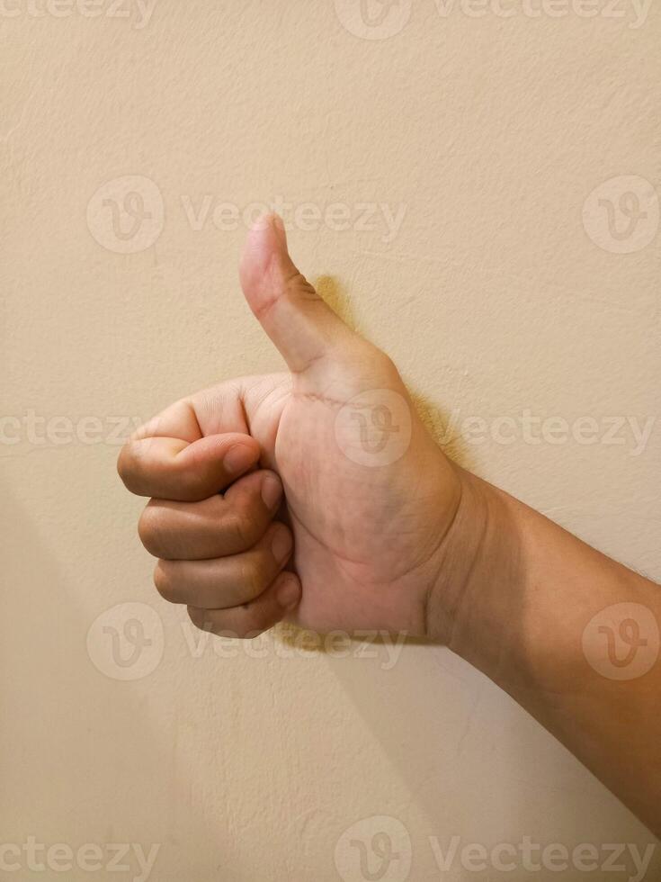 Hand Showing Thumbs Up Against Cream Wall, Approval Sign, Positi photo