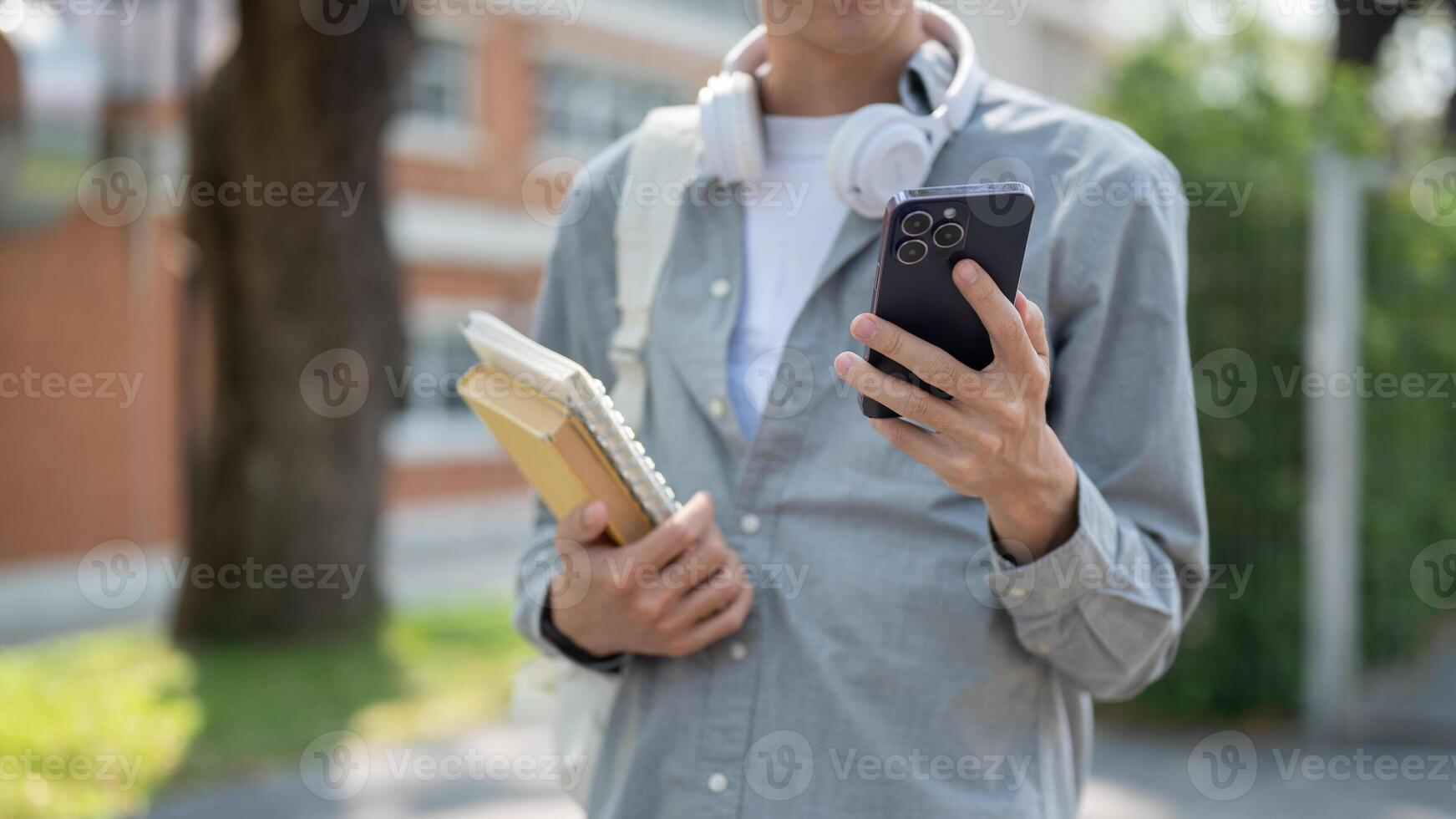 Close up of man looking at smartphone in left hand and books in right hand standing on street. photo
