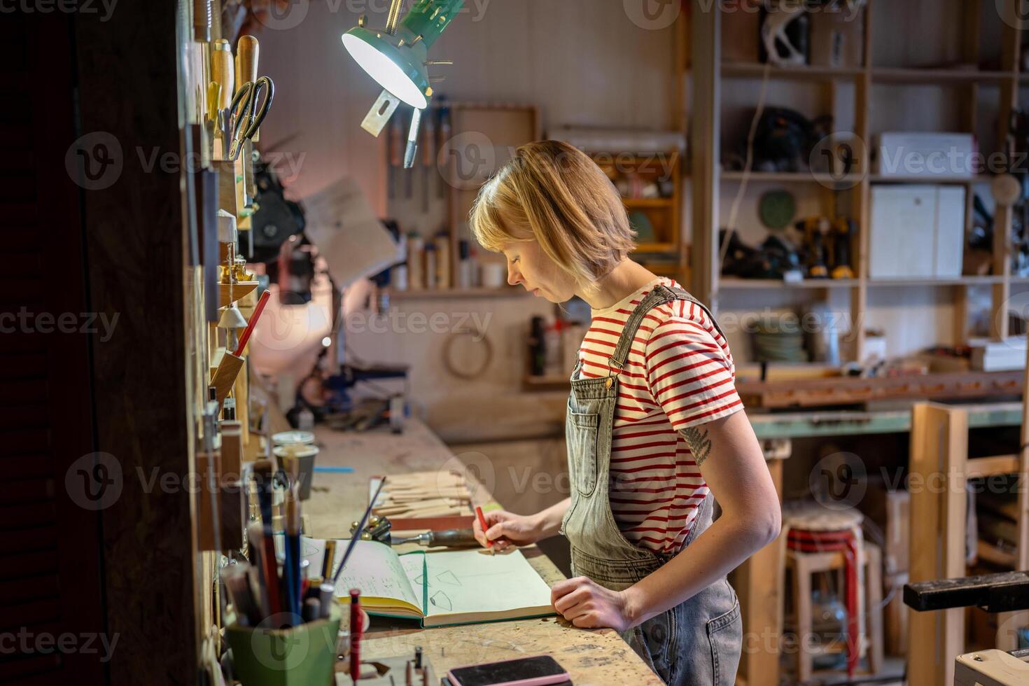 Motivated craftswoman draws sketches of upcoming wooden creations in notebook before starting work photo