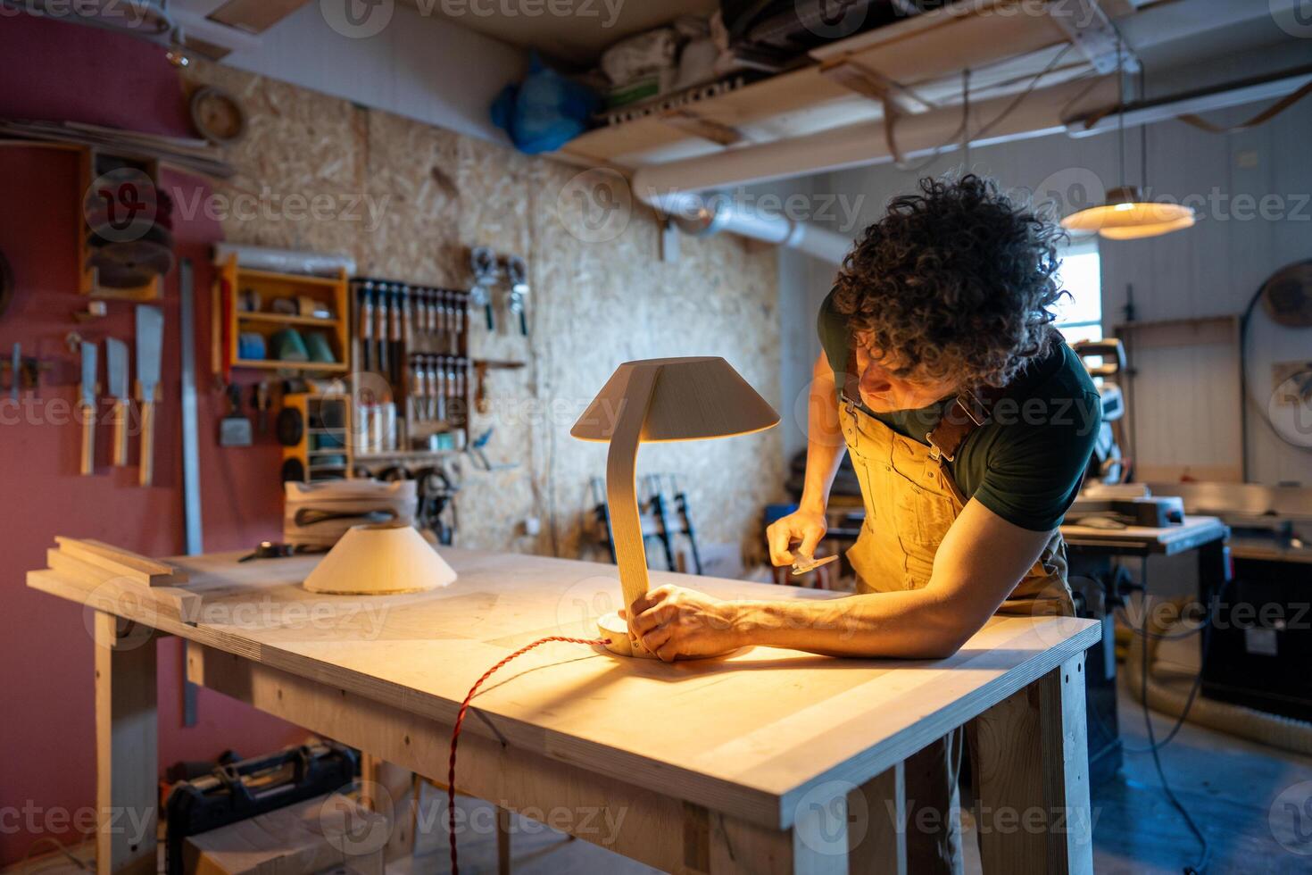 Skilled woodworker examining handmade lamp detail. Checking red wire connection, custom design diy photo