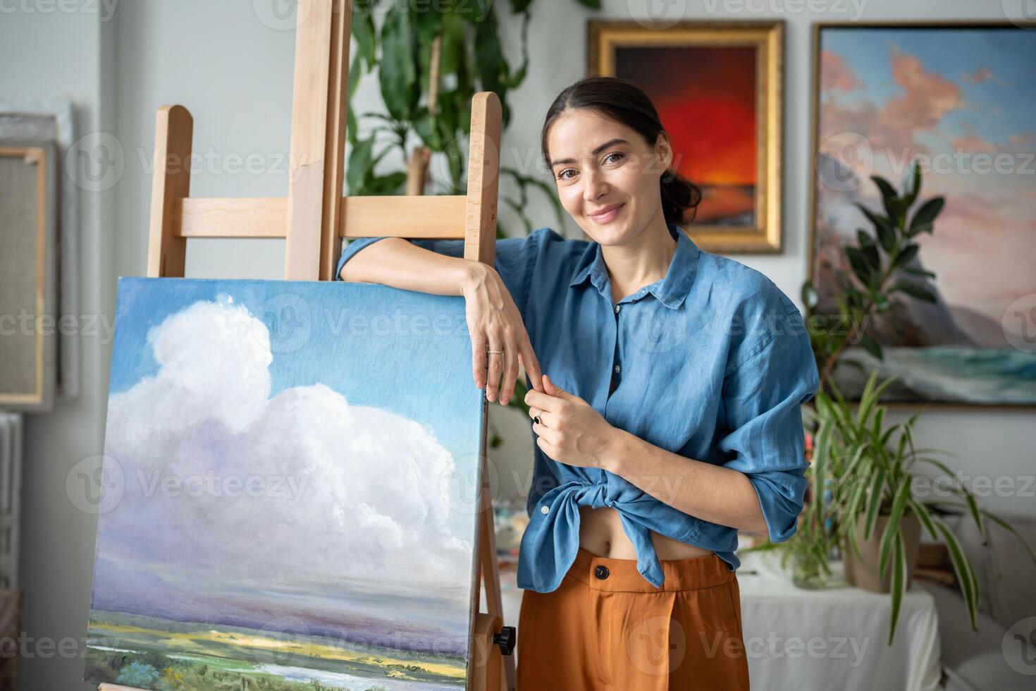 Portrait proud happy woman artist with new painting of sky and nature in workshop, art studio photo
