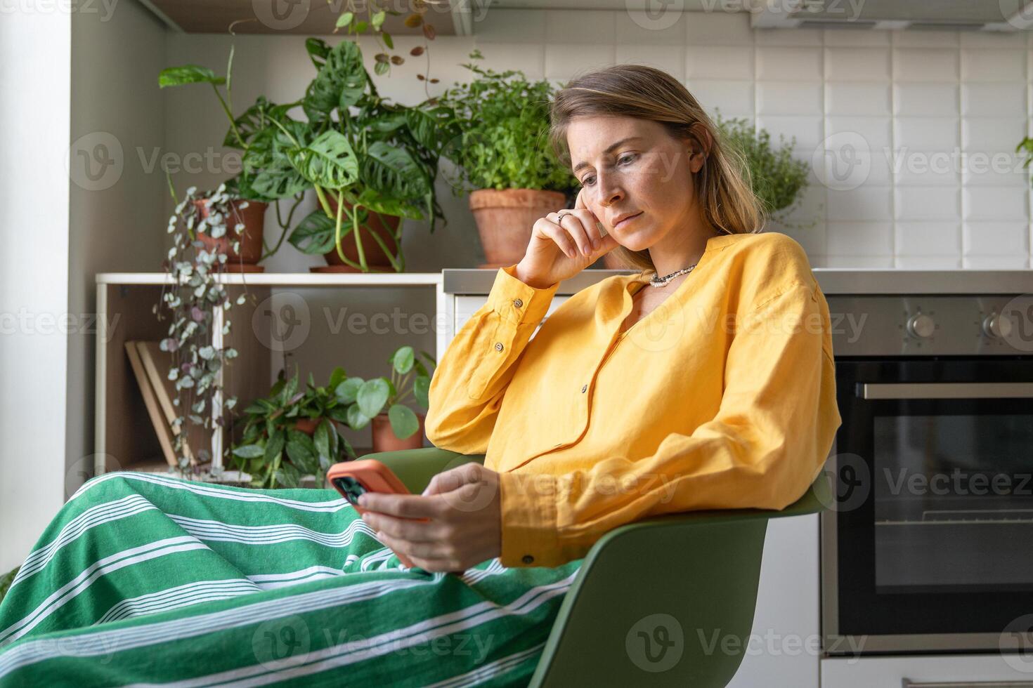Restless woman browsing phone feed checking updates during downtime at home among house plants photo