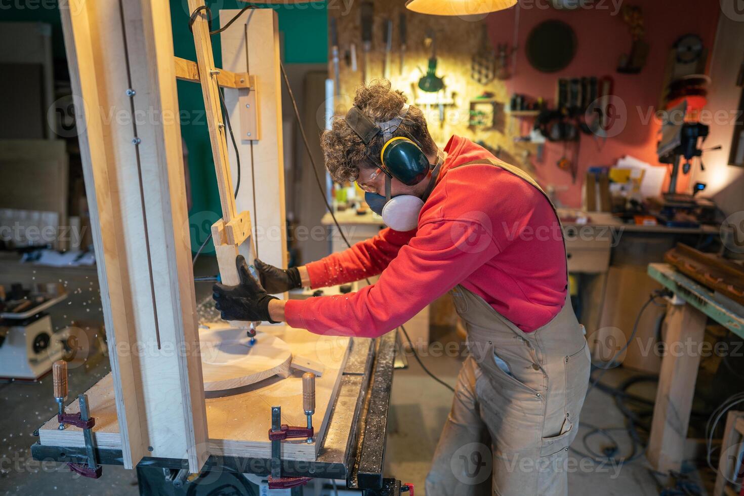 Carpenter in protective gear sands stool foundation in wood workshop. Smooth finishing, sculpting photo