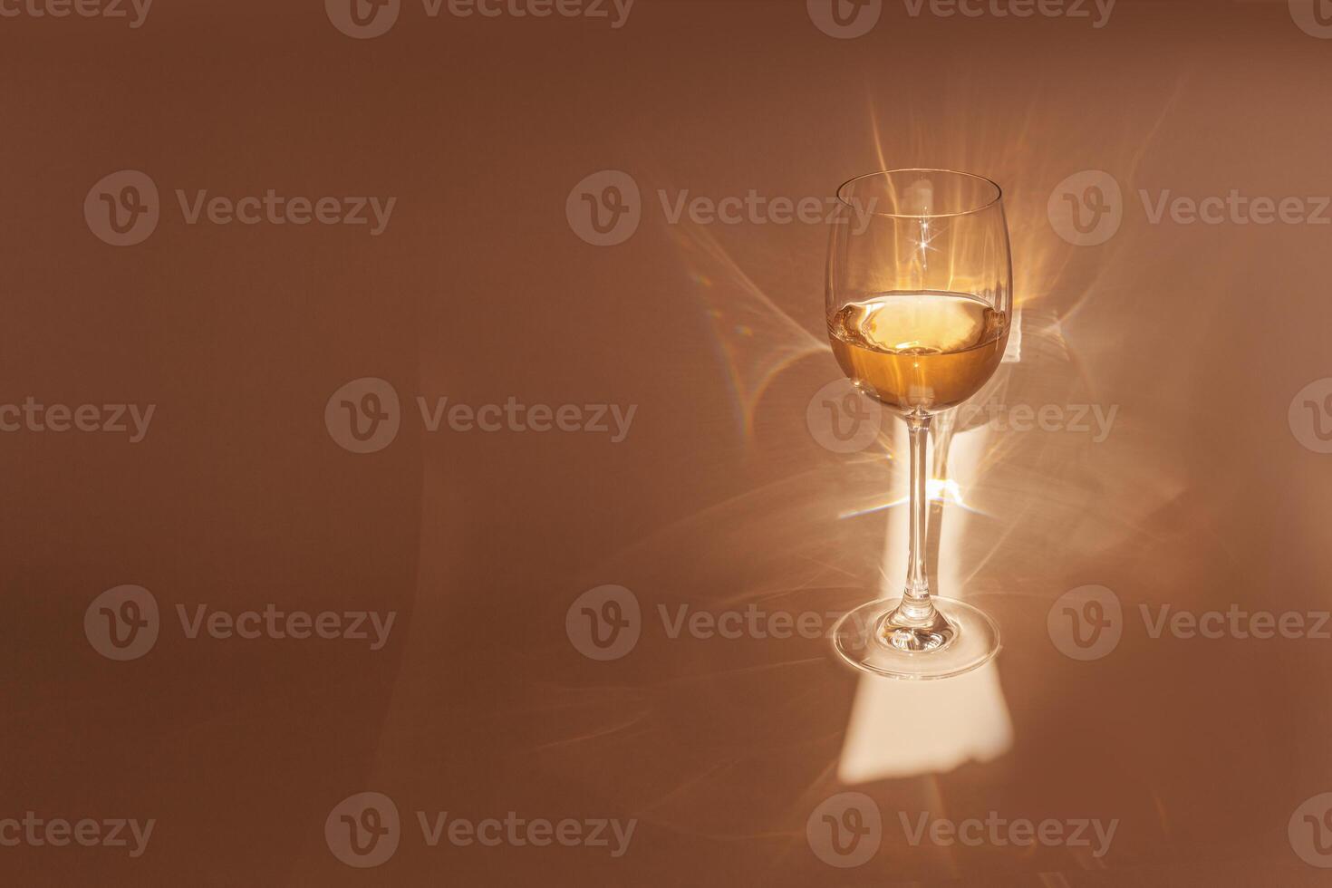 Sunbeam falls on glass of white wine, drink sparkles in sunlight, still life with wineglass of shiny alcohol, beige background with shadow and sun glare, Minimal aesthetic creative photo