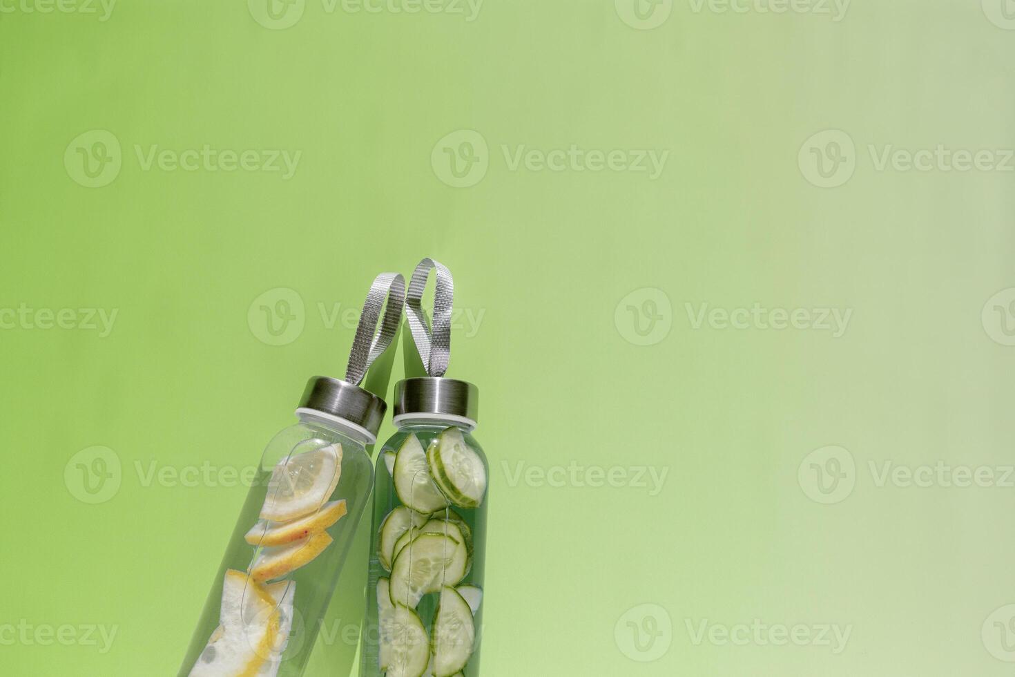 Glass bottles with lemon, cucumber water drink detox at sunlight on green colored background, copy space. Healthy infused water boost metabolism, weight loss. Aesthetic still life, refreshing drinks photo