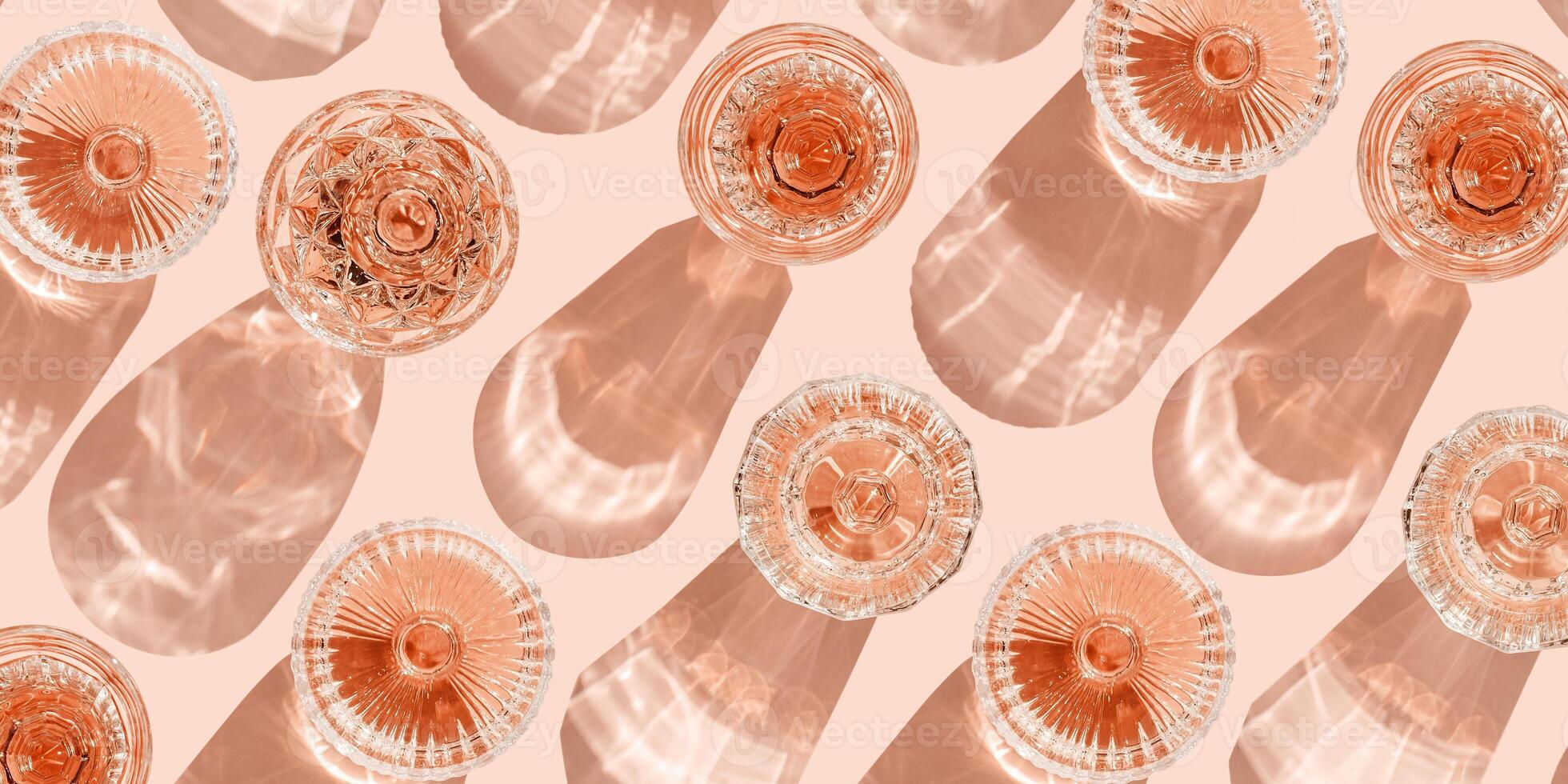 Minimal summer party banner, glasses of rose wine or champagne on pink with shadows and light reflections. Bright shine wineglass with sparkling alcohol drink at sunlight, top view monochrome pattern photo