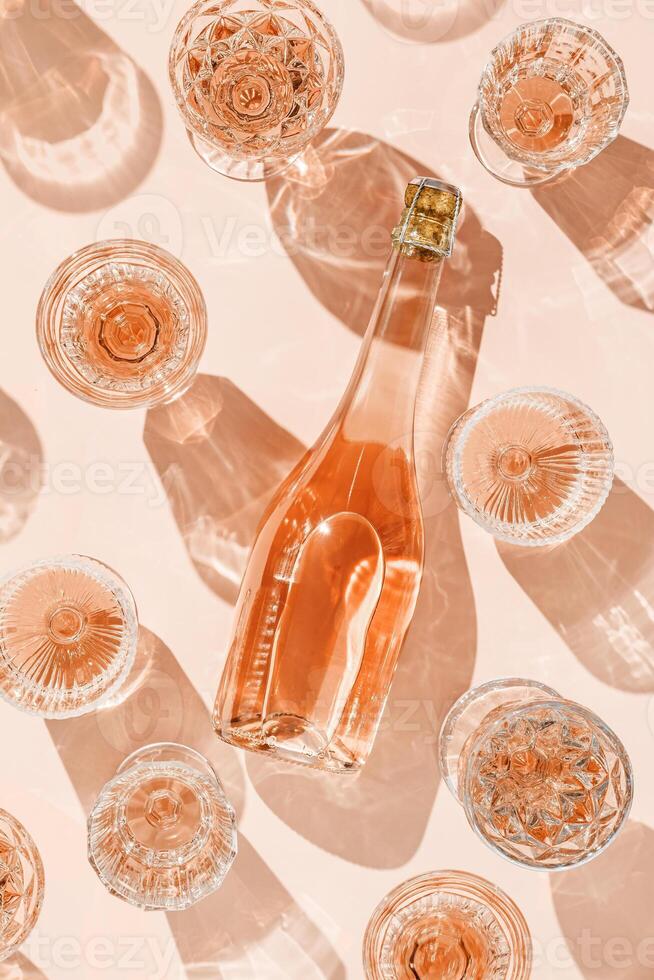 Top view champagne bottle and glasses of rose wine on soft pink background with artistic shadows and sun glare. Aesthetic still life Clear crystal wineglass, close up sparkling drinks, summer parties photo