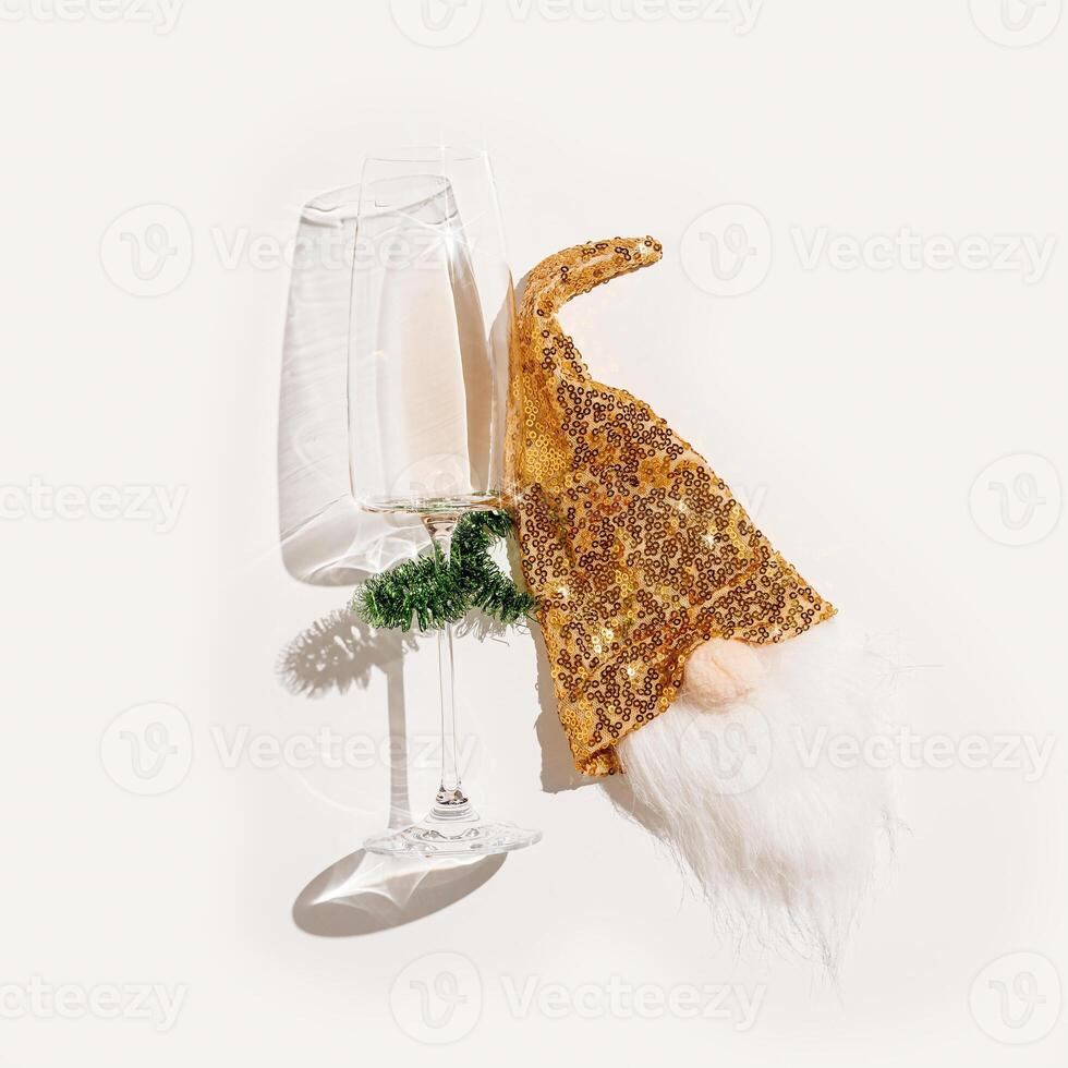 Minimal New Year party concept, flat lay of white wine in champagne glasses, Christmas green tinsel, shiny golden gnome toy for bottle decor, xmas decor. Festive Top view wineglass at sunlight photo
