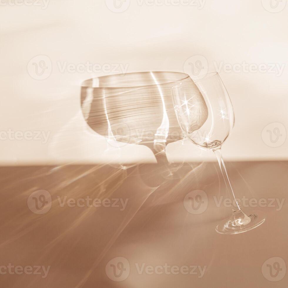 Sunbeams falls on glass for wine, top view glass sparkles in sunlight, still life with shiny wineglass, beige background with shadow and sun glare, Minimal trend aesthetic creative photo, empty space photo