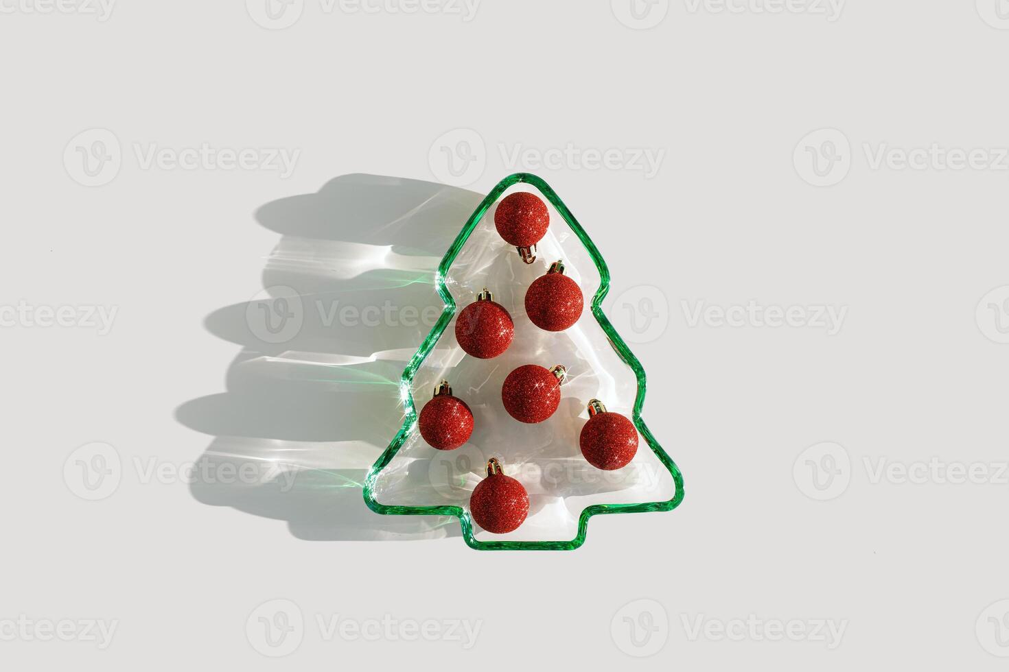 Plate as New Year tree with glittering red Christmas balls on white, Top view Christmas tree from green glowing glass. Natural Sunlight, sparkling holiday food, minimal xmas trendy still life photo
