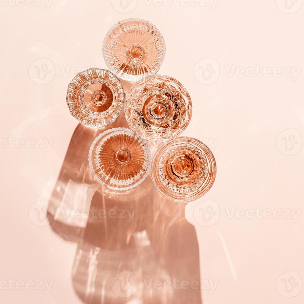 Minimal summer party concept, set glasses of rose wine or champagne on pink with shadows and light reflections. Bright shine wineglass with sparkling alcohol drink at sunlight, top view monochrome photo