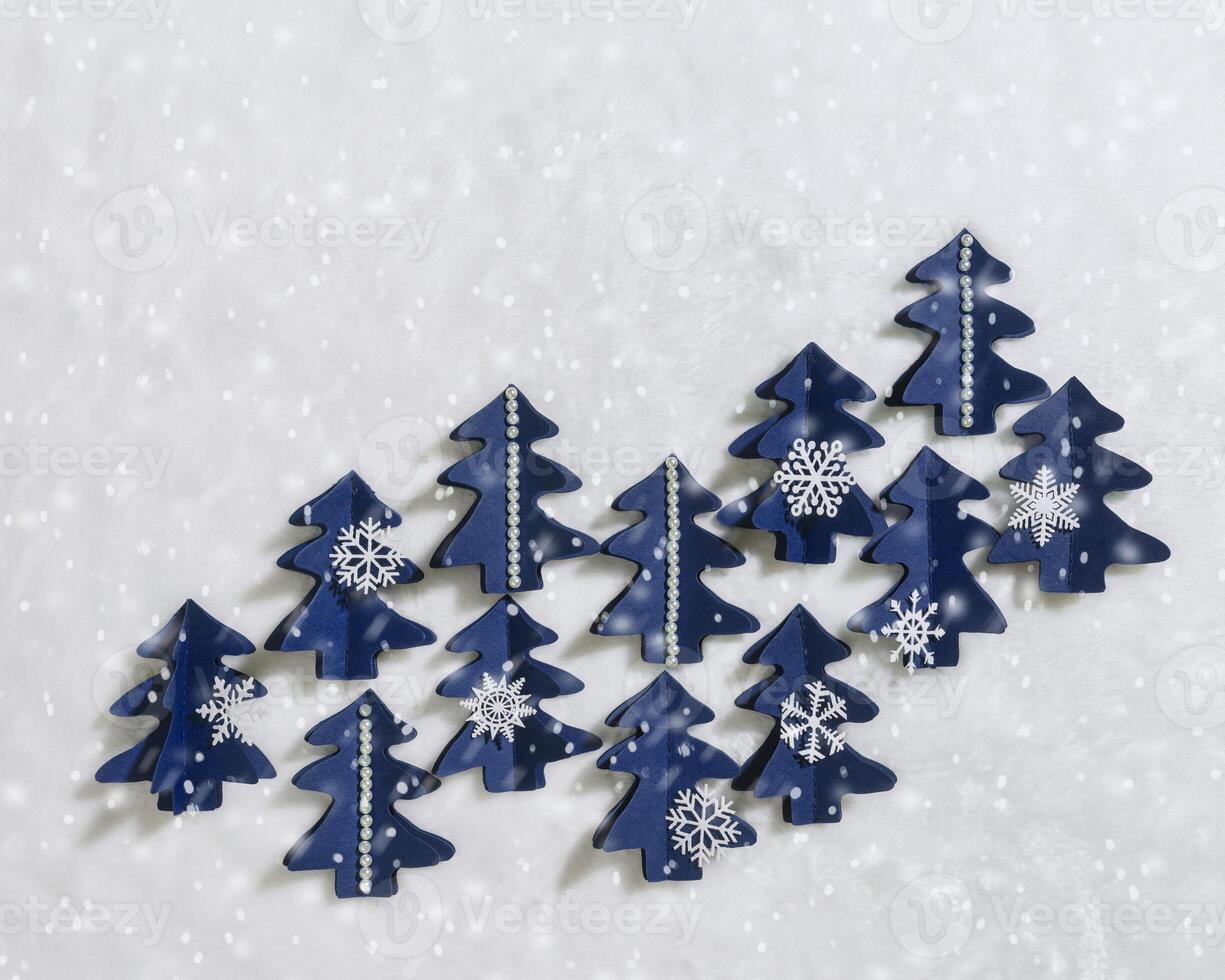 Christmas craft background with handmade blue xmas trees cut out of paper on white fur, firs decorated snowflakes, pearls, snow. DIY eco friendly sustainable christmas decoration, top view flatlay photo