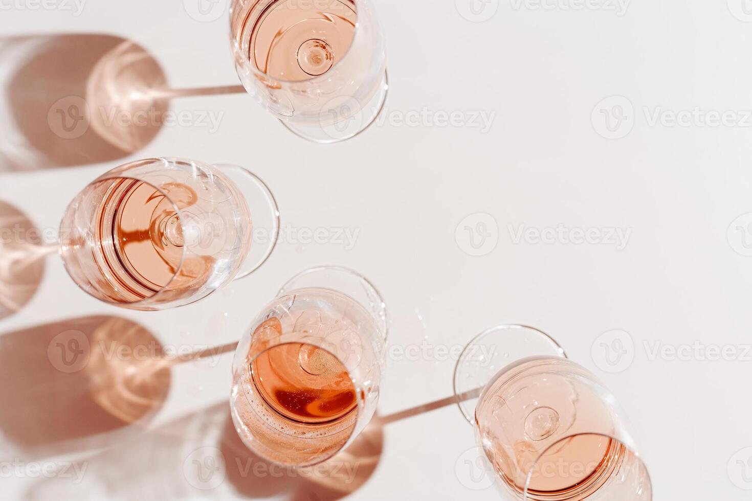 Set of glasses of rose wine at wine tasting, Minimal trend concept. Top view crystal wineglass standing at sunlight, shadow and sun glare, beige pink colored, alcohol drink background, copyspace photo