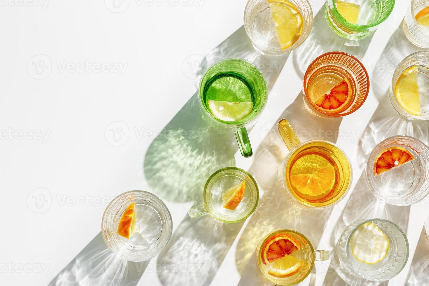 Colorful glass cups of citrus water with slices of fruit, bright glasses of detox drink with beautiful shadow at sunlight, minimal style aesthetic top view, creative summer drink pattern, copyspace photo