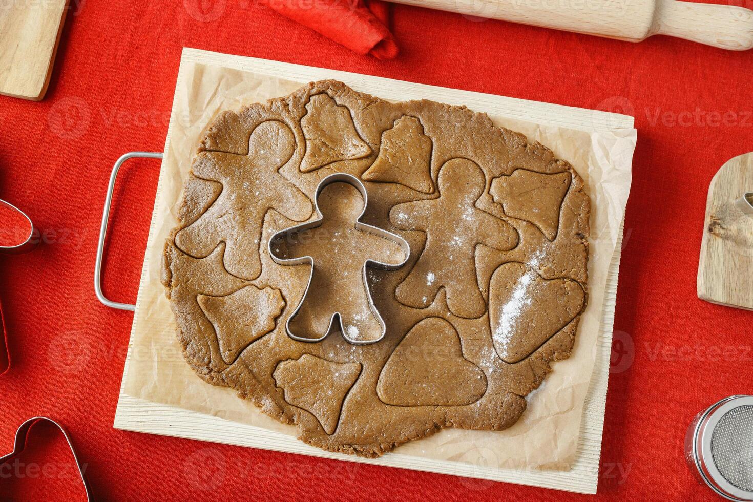 Preparation Cooking ginger cookies on red linen tablecloth background, Christmas and New Year holiday cookies in varios shapes, cutting biscuits with metal cookie cutters, wooden rolling pin photo