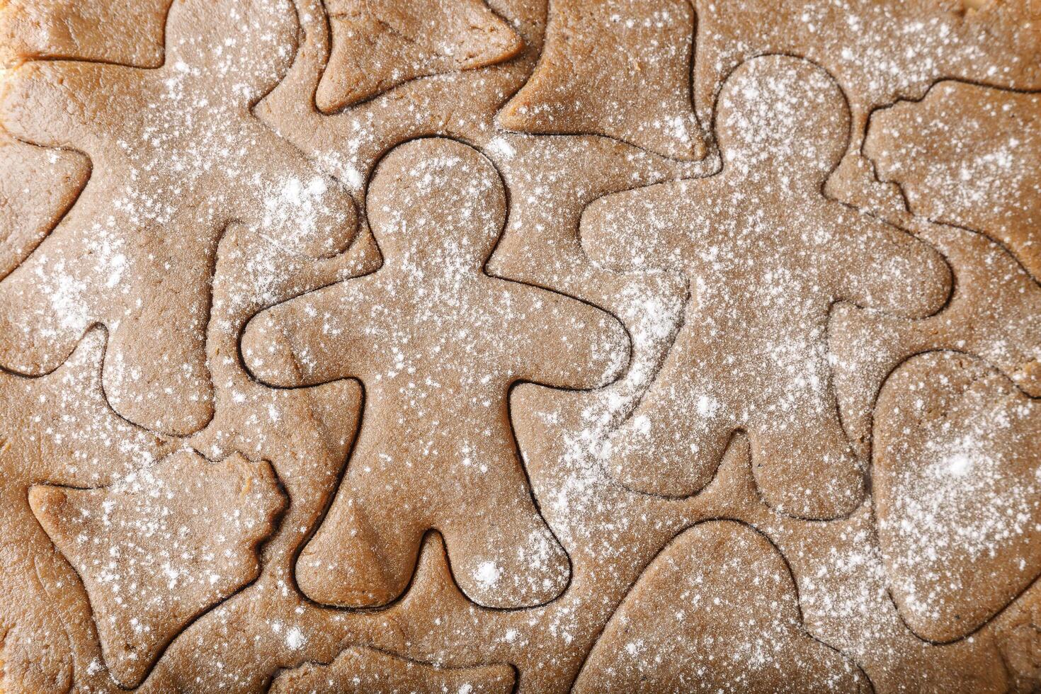 Cooking ginger cookies, Christmas and New Year traditional cookies in shape of gingerbread man, raw rolled out dough with cut out dough figures, closeup texture, top view, pattern on dough, above photo