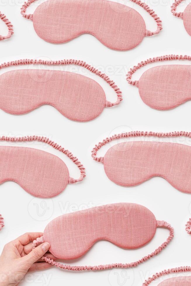 Minimal pattern from pink textile sleep masks on white light background. Woman hand take eye mask, comfort rest and quality sleep concept. Creative aesthetic top view composition photo
