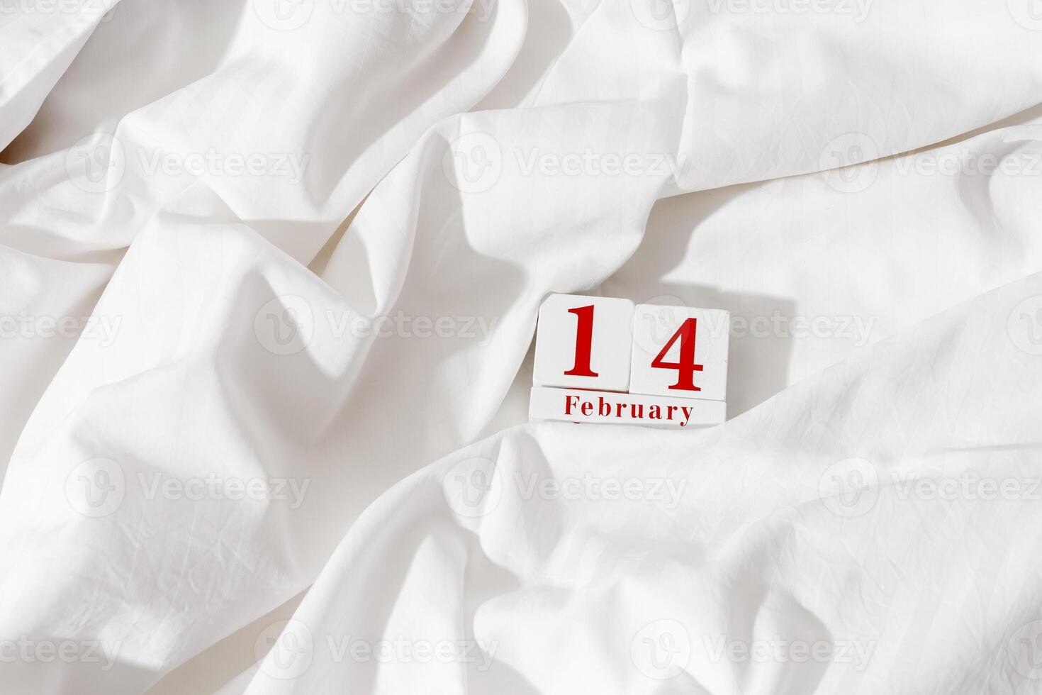 14 february background, holiday date on calendar in bed with white cotton sheets. Valentine's Day minimal concept, aesthetic lifestyle photo. Wooden calendar with red text, festive romance date photo