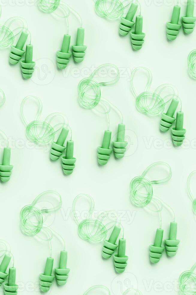 Reusable silicone green earplugs, for swim, sleep, rest as minimal trend pattern on light green background. Soft, flexible ear plug on cord against noise, protect hear, top view, flat lay photo