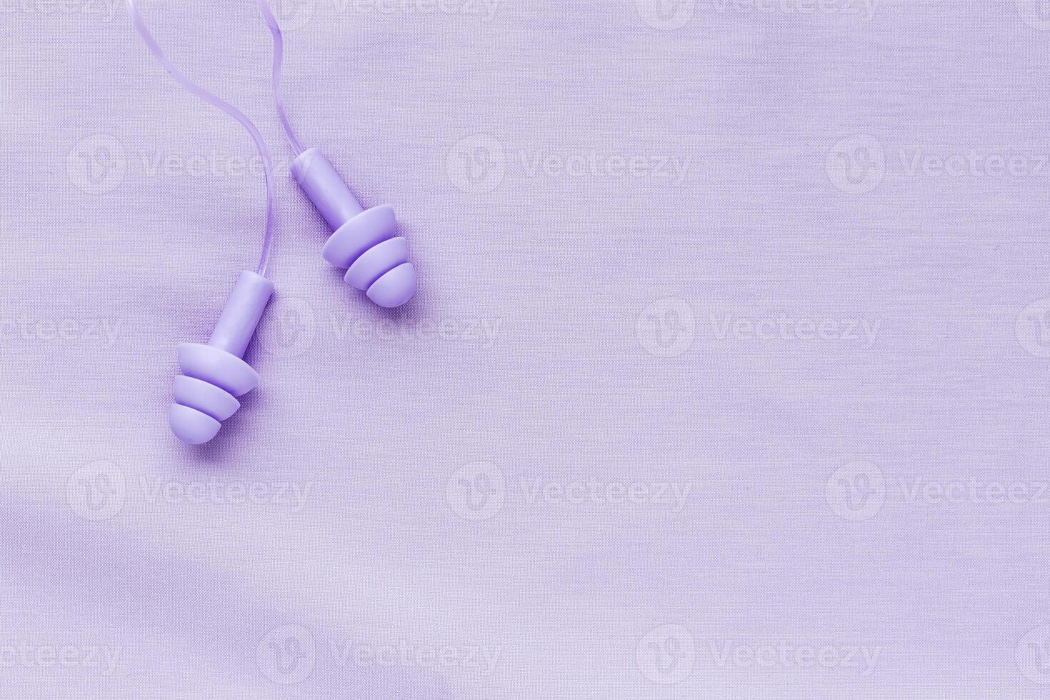 Reusable silicone earplugs purple color on colored cloth background, copy space. Soft, flexible ear plug on cord, for swim, sleep, against noise, protect hear, monochrome top view, minimal style photo