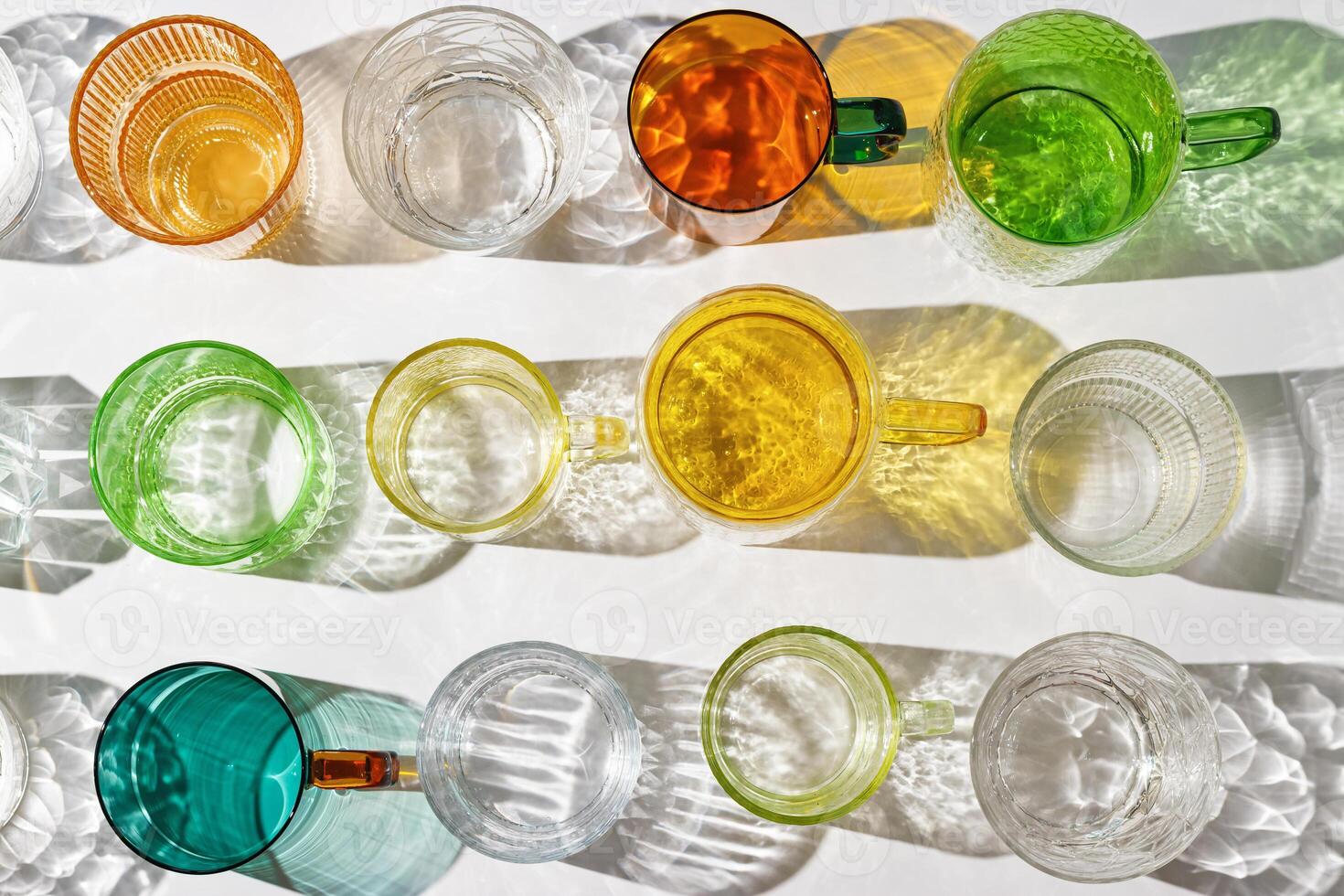 colored glass cups from transparent and clear glasses with beautiful shadow at sunlight, summer drink for events or relaxation, minimal aesthetic top view, creative summer drink backdround photo