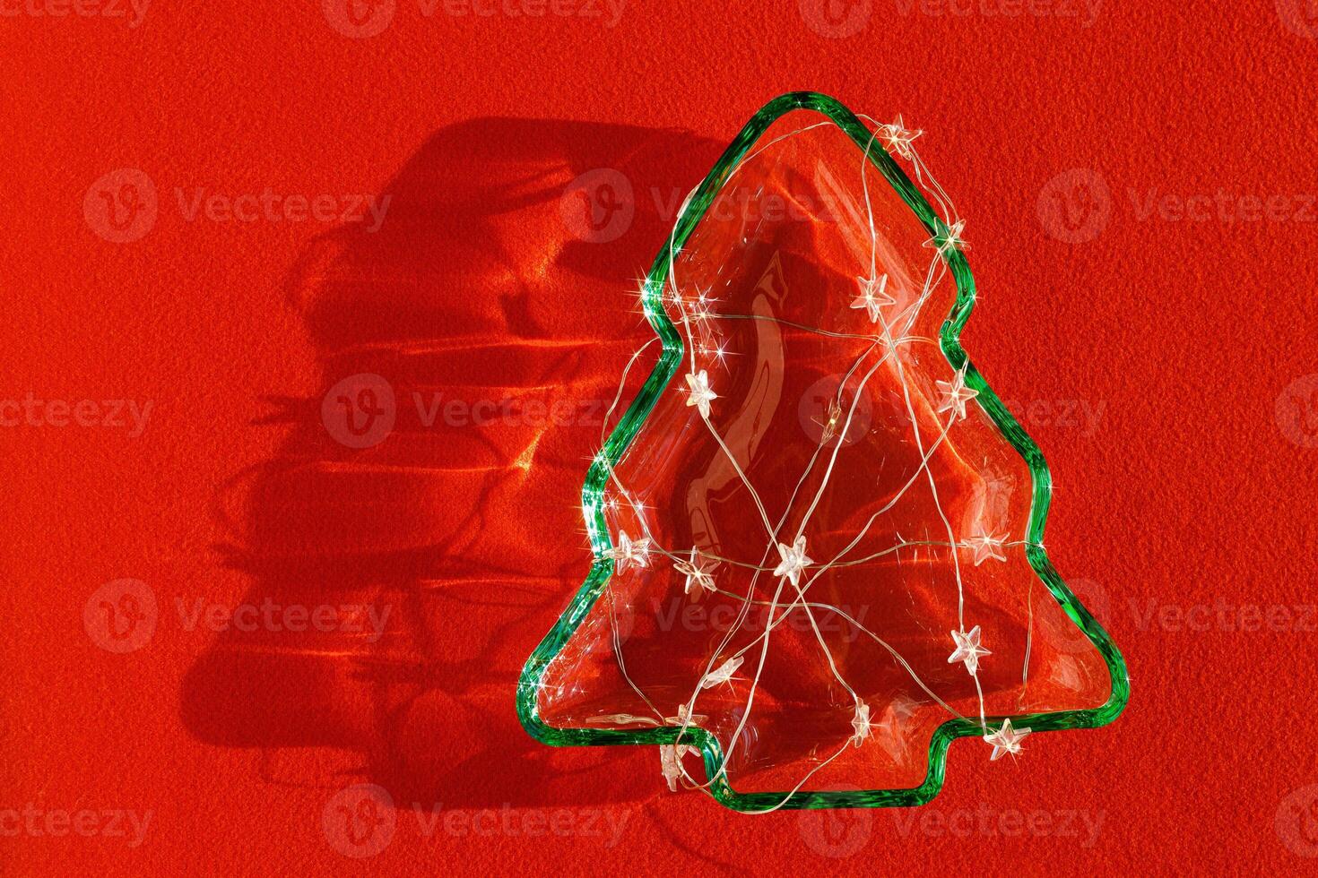Plate as New Year tree with Glowing light stars garland on red textile, Christmas tree from transparent green glowing glass glare. Sunlight and shadow, sparkling holiday dish, xmas still life photo
