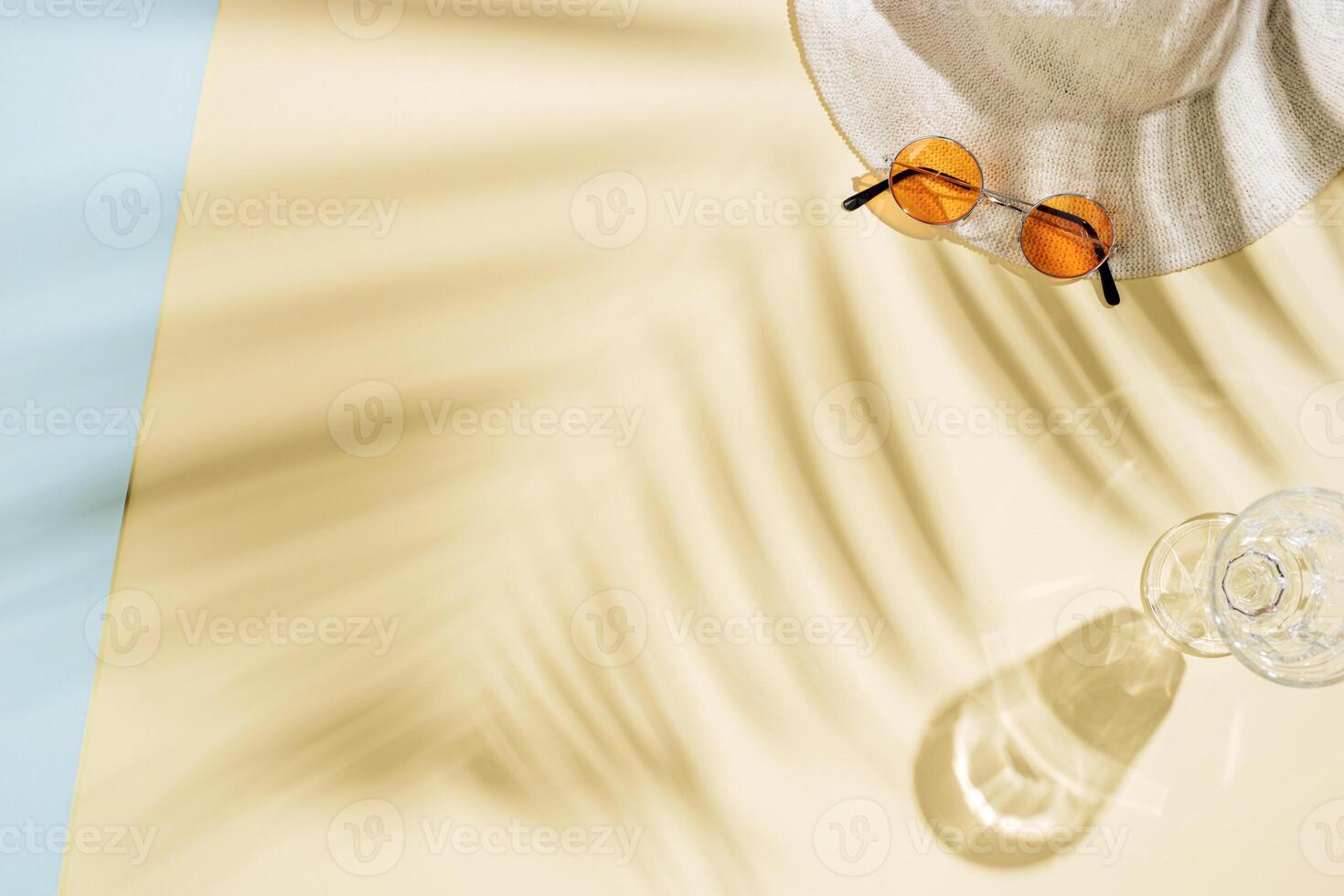 Summer beach rest concept background with sun hat, glass of water with palm tree shadows photo