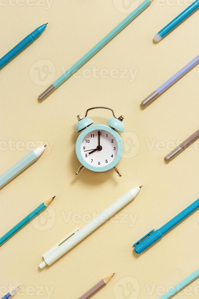 Creative Flat lay with clock and geometric pattern from blue pens and pencils on beige Time to go to school concept photo