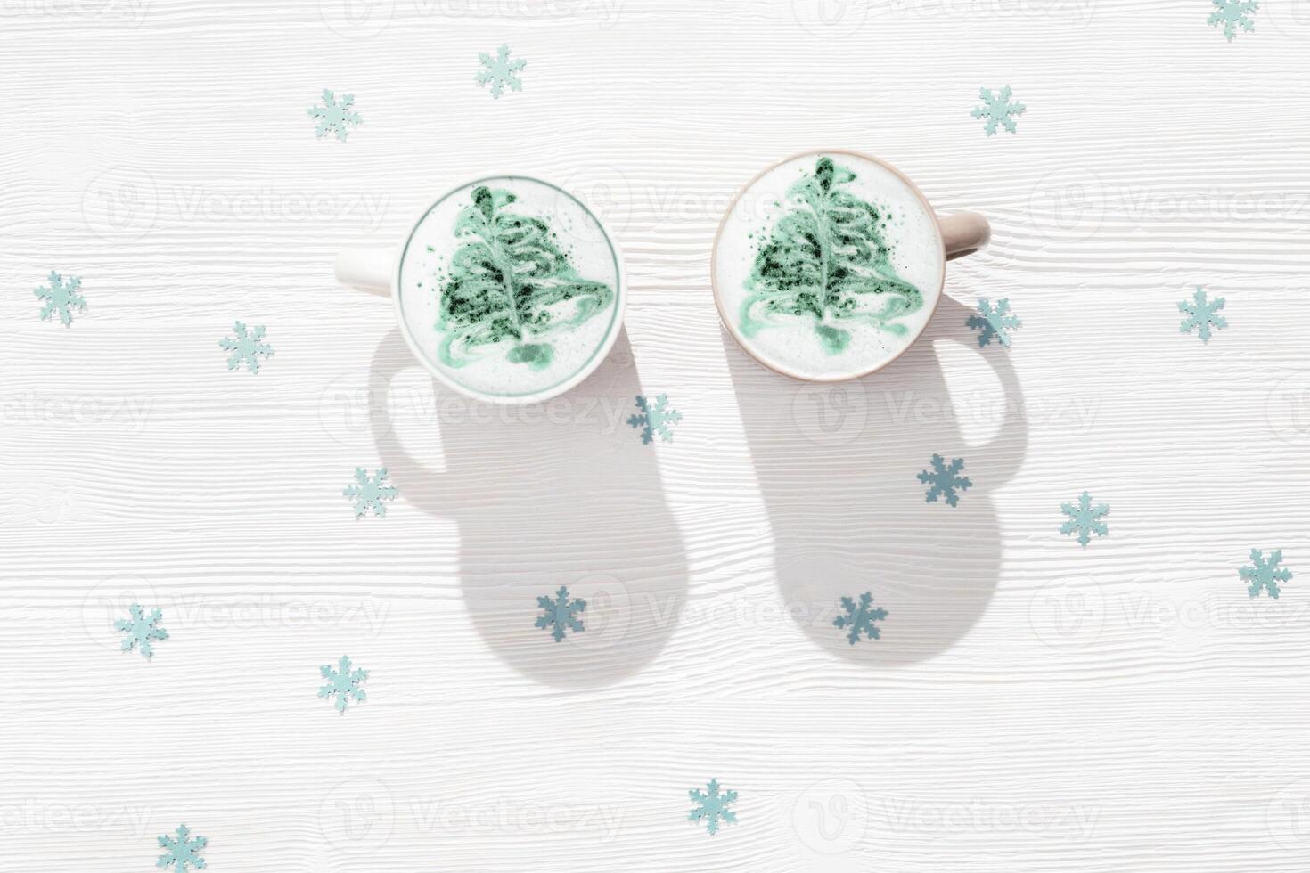 Latte winter coffee with New year tree art in big mug on white table with blue paper decor snowflakes. photo