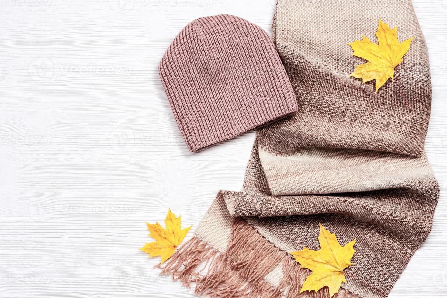 Autumn comfortable clothes and decorative yellow maple leaves. Scarf and cap for woman photo