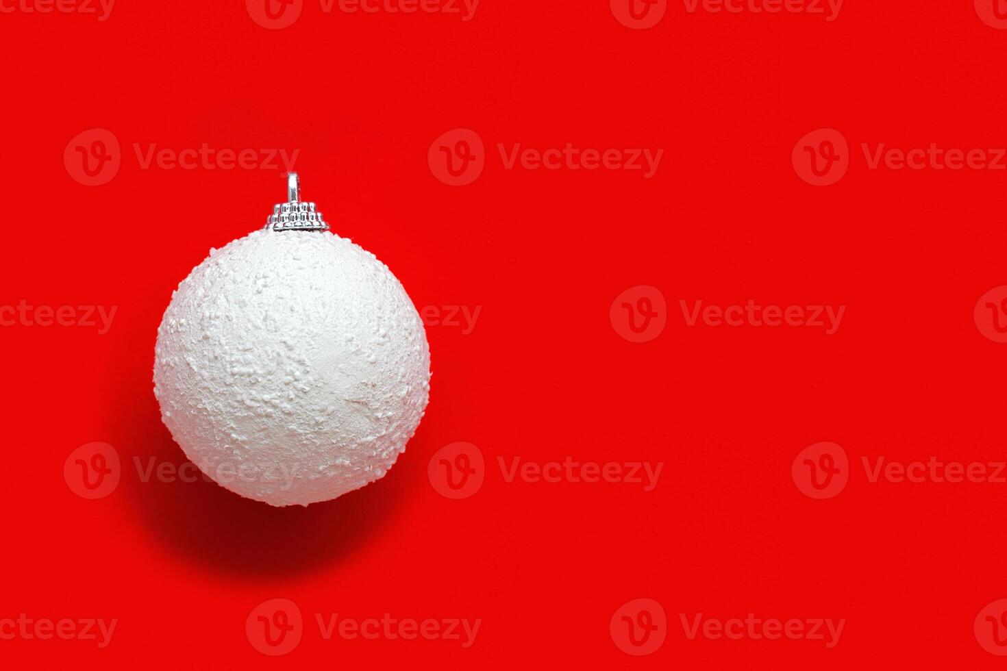 White New years ball from snow, holiday toy on bright red. Christmas greeting card. Minimal style photo
