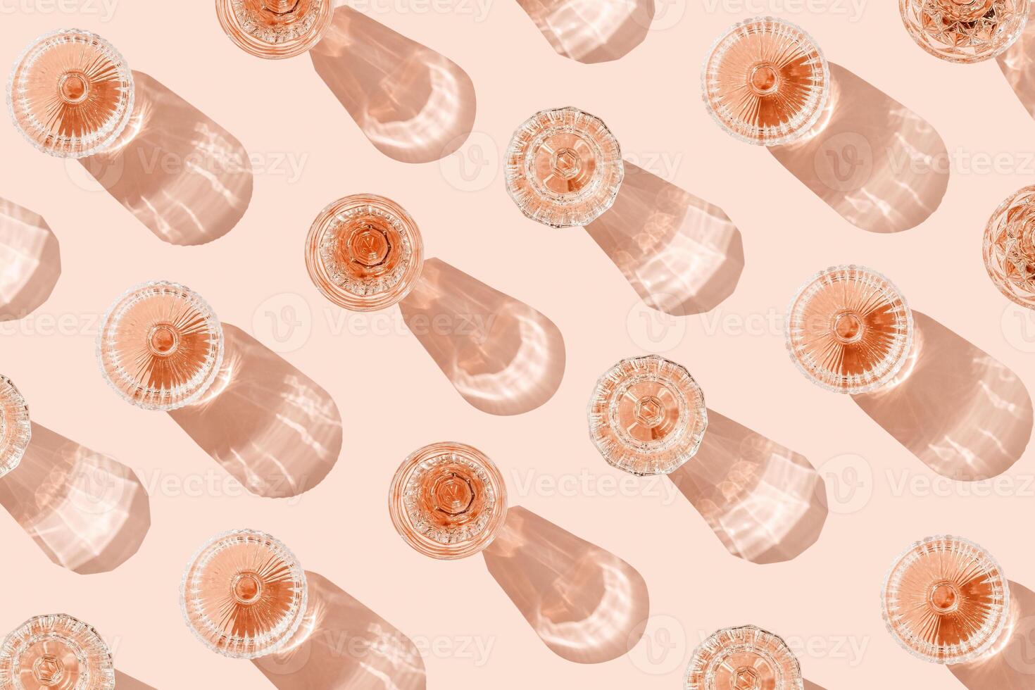Minimal summer event concept, glasses of rose wine or champagne on pink with shadows and light reflections. Bright shine wineglass with sparkling alcohol drink at sunlight, top view monochrome pattern photo