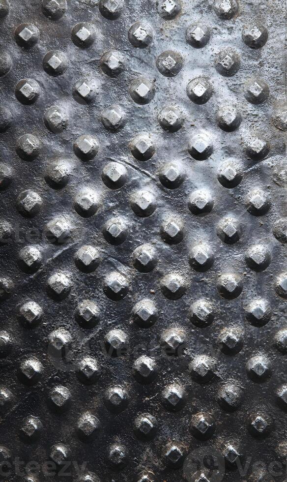 Textured metal surface with raised circular and square elements creating a tactile and visually interesting pattern with industrial feel photo