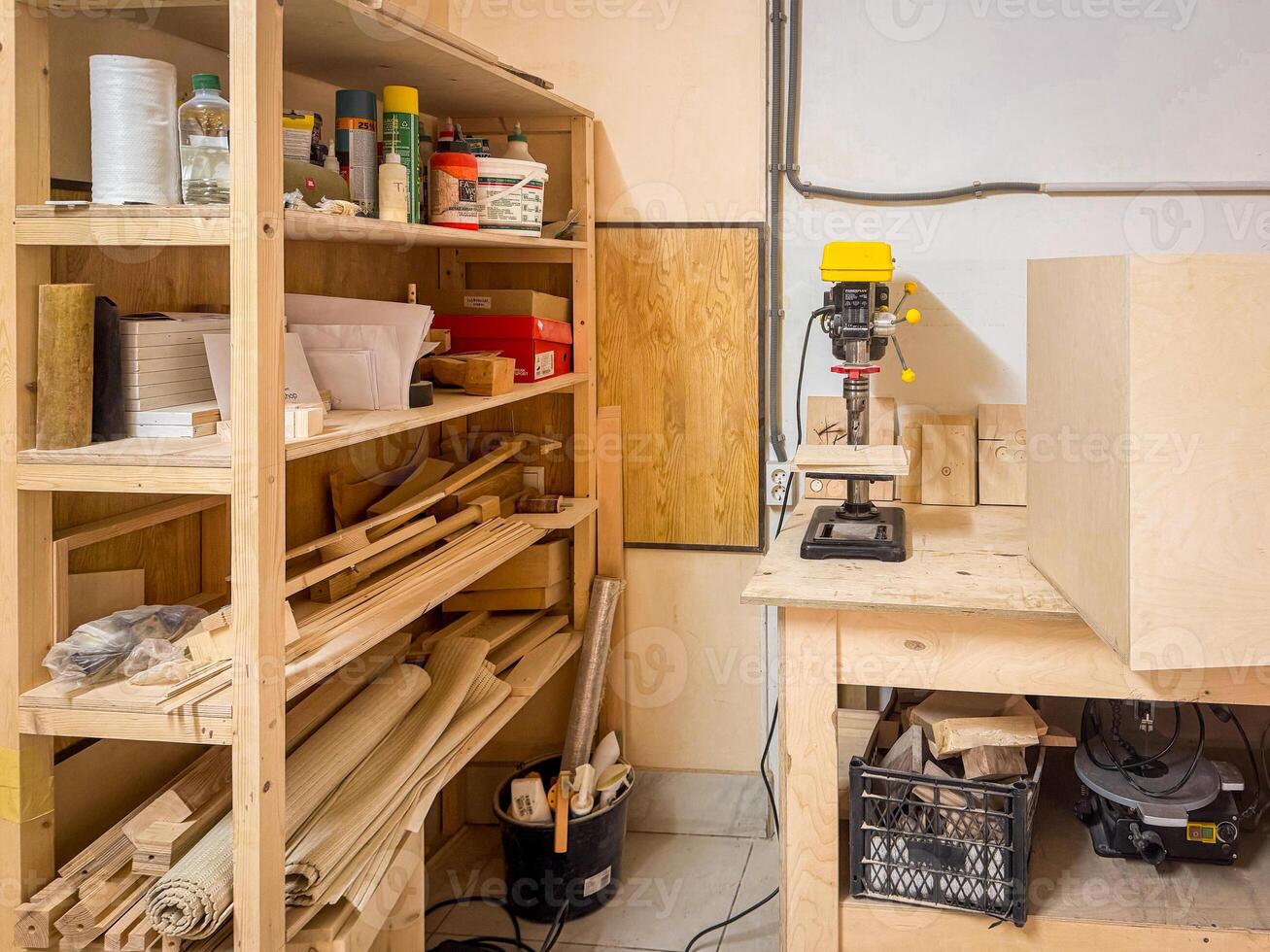 Organized woodworking shop featuring tools, drill press, materials, and shelving packed with supplies, set in a clean and functional creative workspace photo