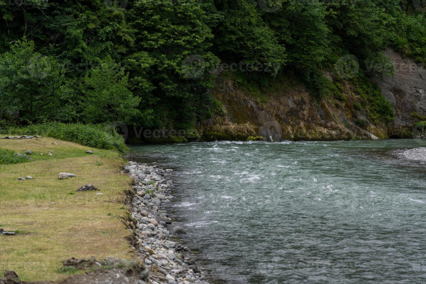 a river, a stone bank and a field on the background of a mountain photo