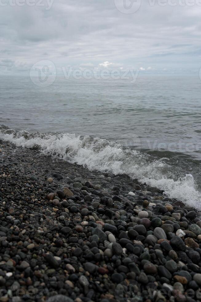 Wave on a stone beach in Batumi, cloudy sky photo