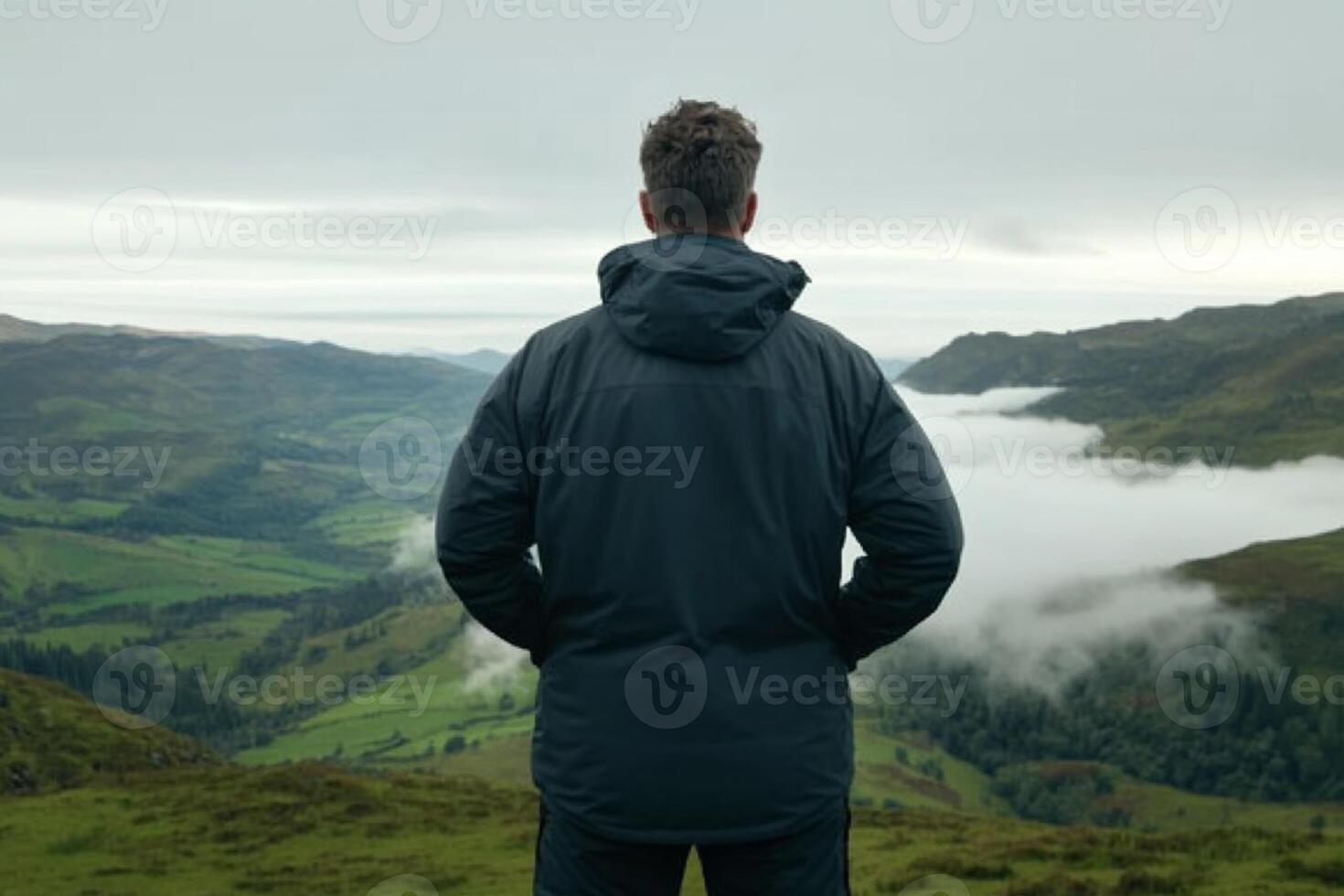Man in black jacket standing on top of mountain overlooking valley photo