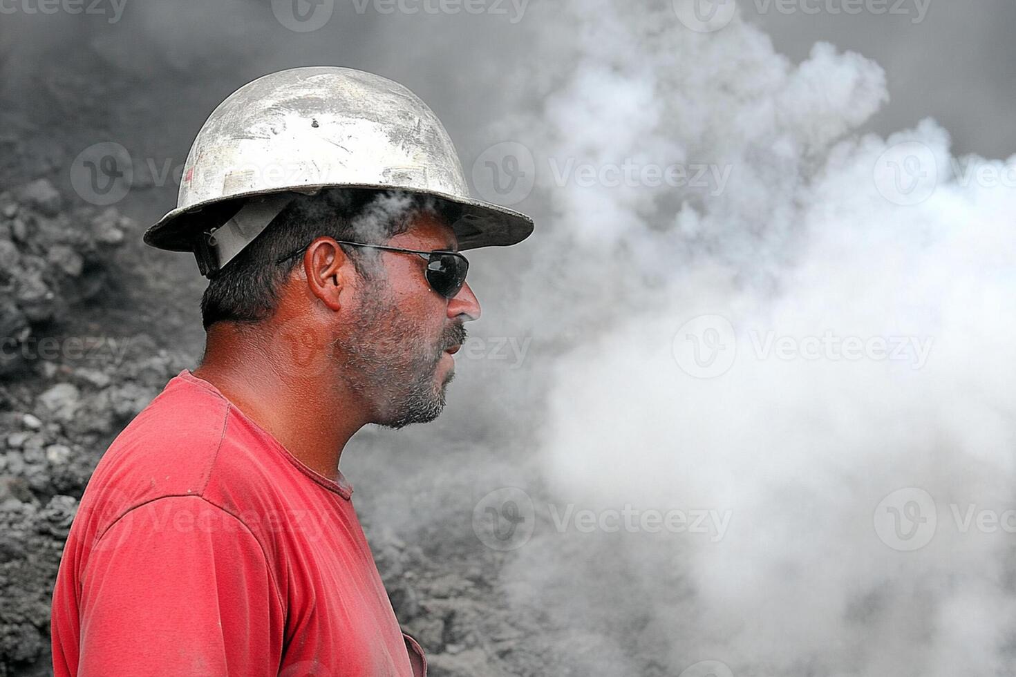 A man wearing a hard hat and sunglasses is standing in front of a pile of coal photo